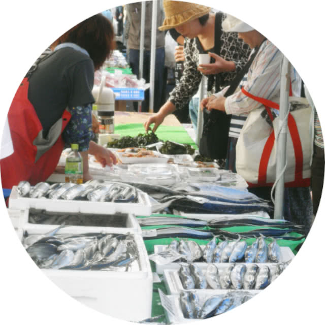 日本の市場で新鮮な魚を販売する様子。客が魚や海藻を選びながら店員とやり取りしている。